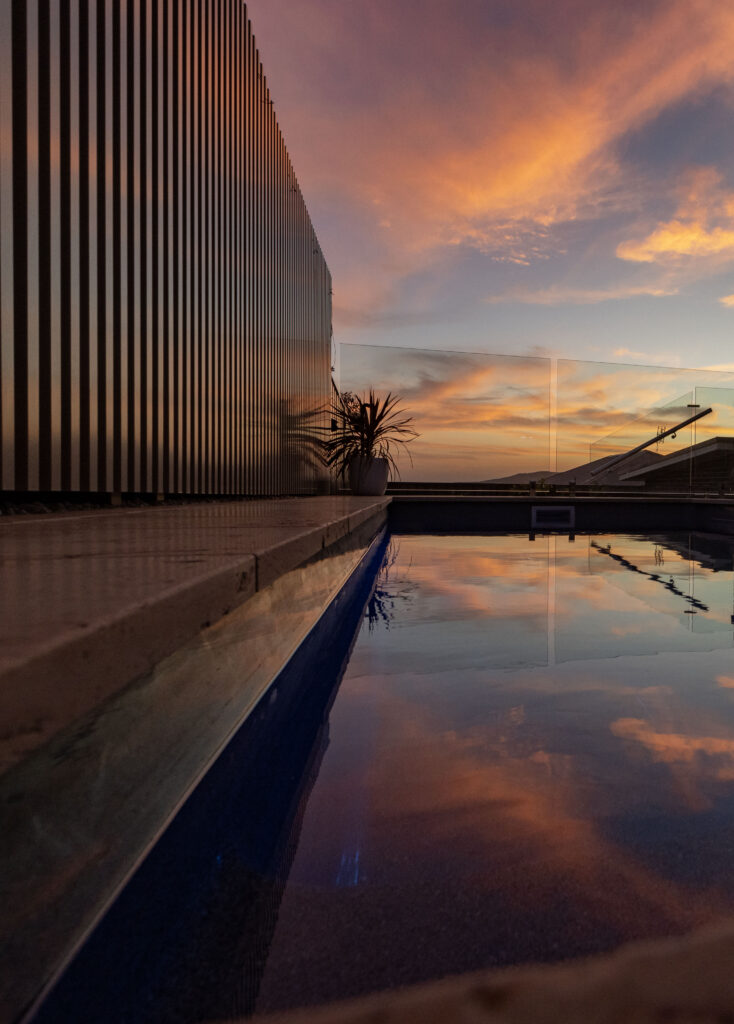 Pool surrounds landscaping project in Cameron Park with sandstone feature wall, decking, glass pool fencing, and travertine pool surrounds. 