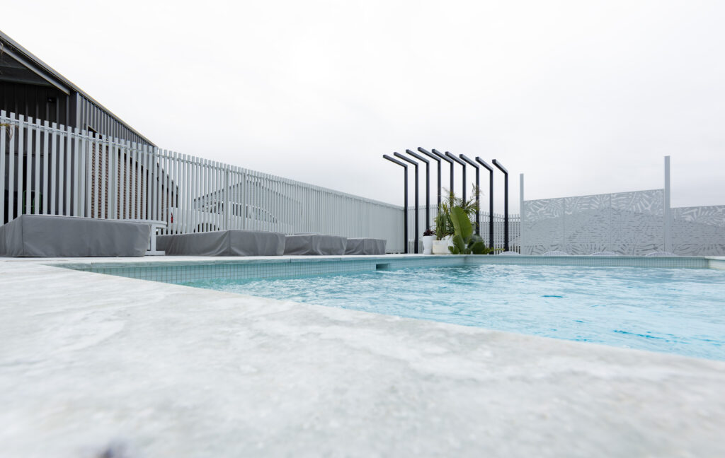 Completed pool surrounds landscaping project in Louth Park, including pool surround paving, decorative screening, glass pool fencing, and planting. 