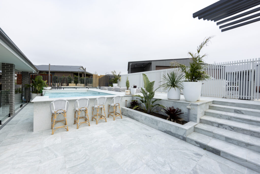 Completed pool surrounds landscaping project in Louth Park, including pool surround paving, decorative screening, glass pool fencing, and planting. 