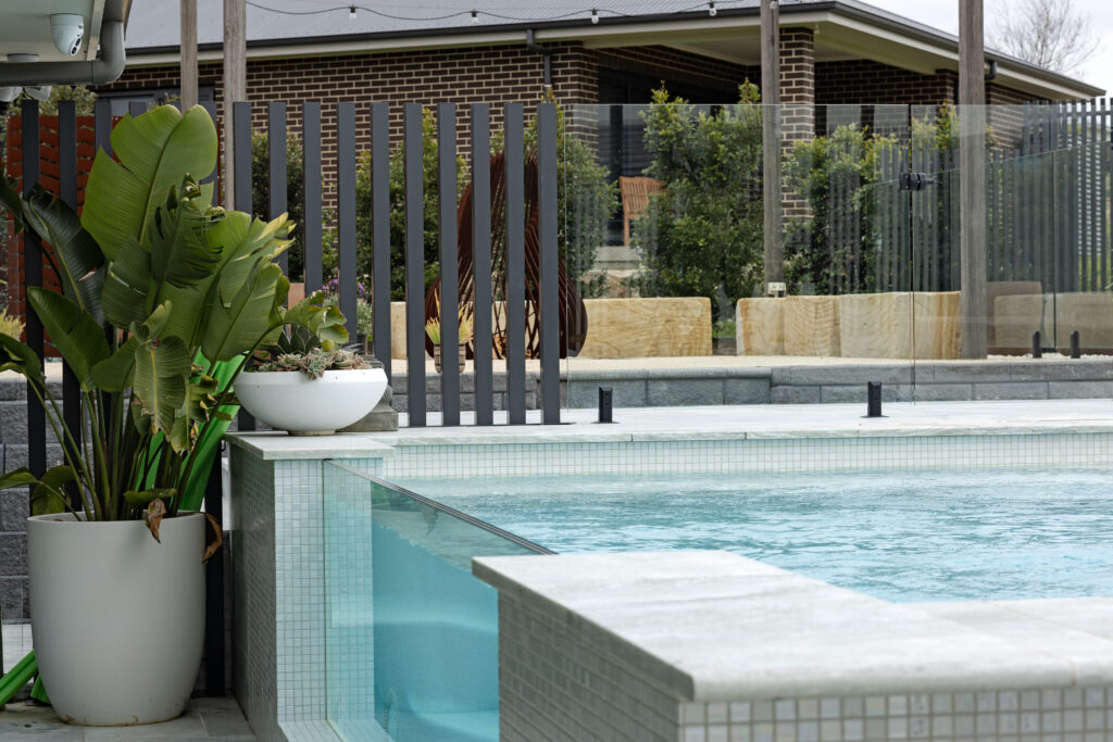 Completed pool surrounds landscaping project in Louth Park, including pool surround paving, decorative screening, glass pool fencing, and planting. 