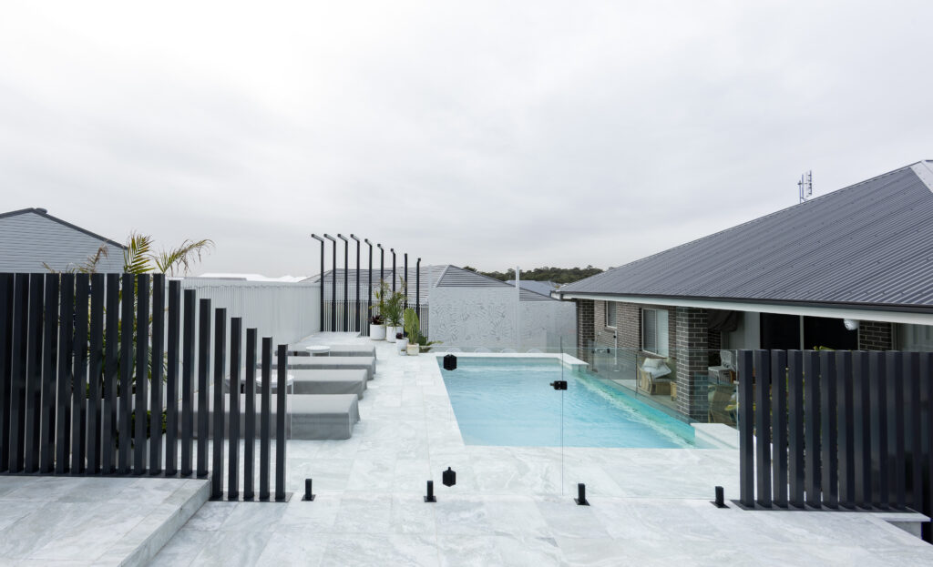 Completed pool surrounds landscaping project in Louth Park, including pool surround paving, decorative screening, glass pool fencing, and planting. 