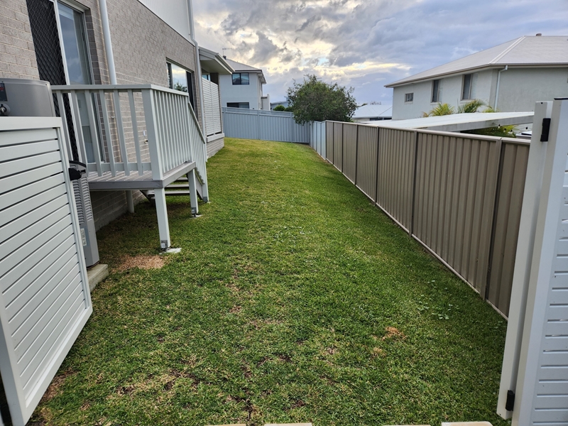 Side yard before landscaping in Corlette, narrow lawn strip beside the home and deck stairs