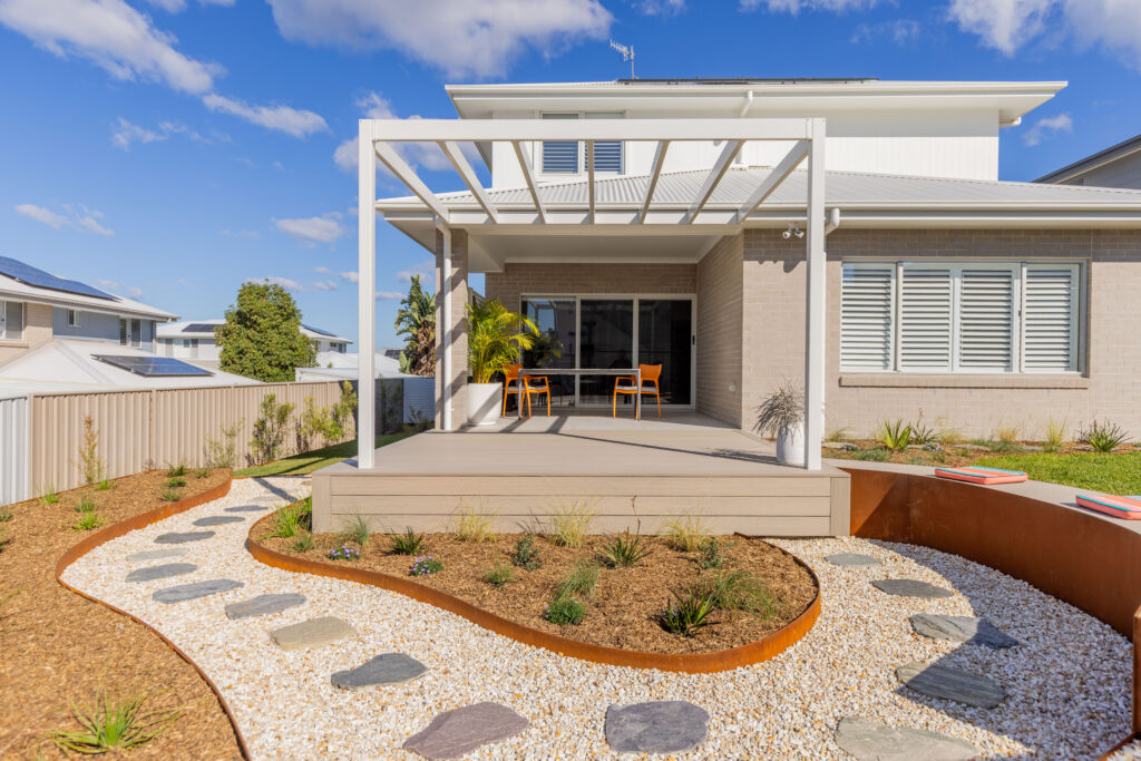 Outdoor deck and pergola seating area in a Corlette native garden design, with curved garden bed and stepping stones