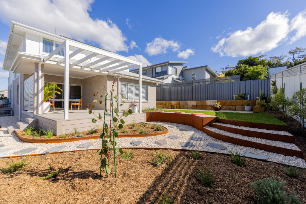Finished native garden design Corlette rear yard with deck, pergola and tiered corten steel garden beds