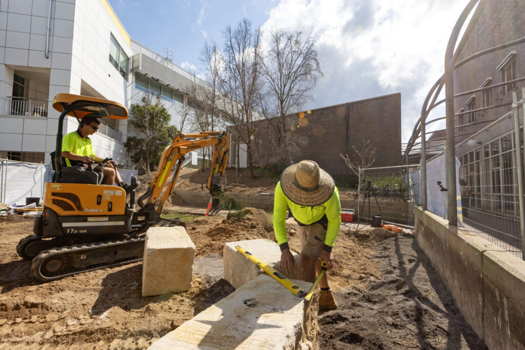 Worker levelling a sandstone log during construction of the John Hunter Hospital cultural connection space