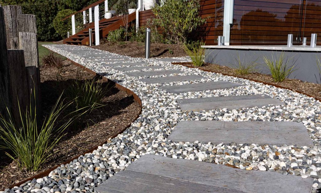 Concrete sleeper pathway edged in Corten steel, leading through gravel toward the deck stairs