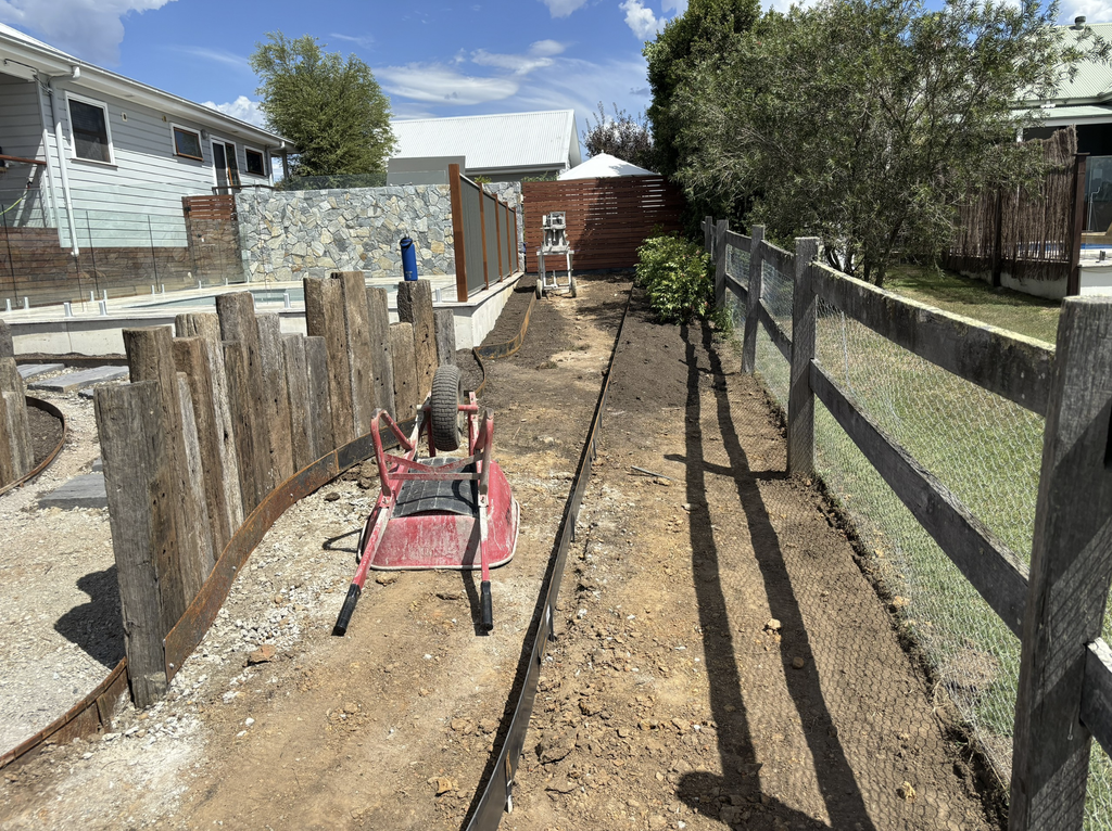Recycled hardwood railway sleepers being installed as a wind barrier beside the pool area in Pokolbin