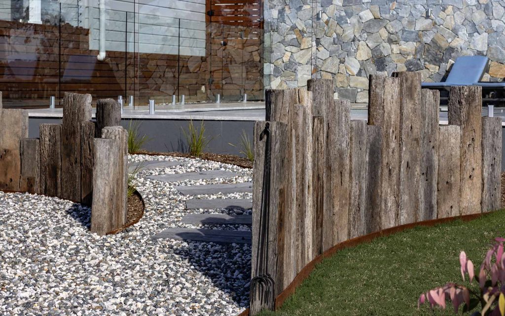 Vertical railway sleeper privacy screen with a garden gate leading to a gravel and stepping stone path