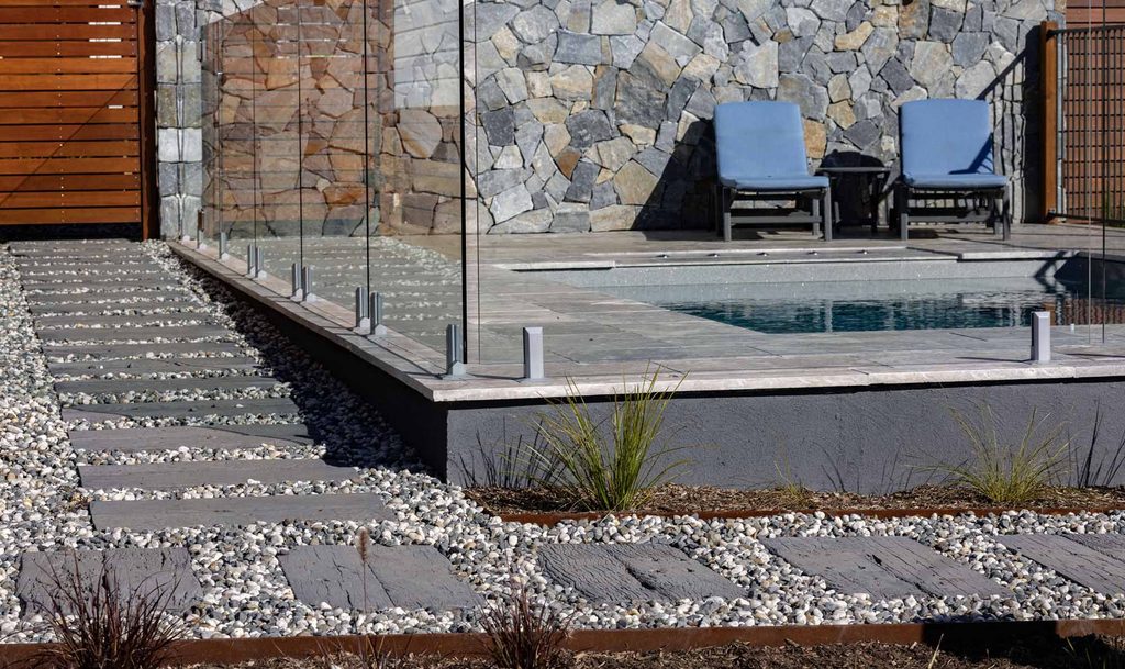 Concrete sleeper stepping stones meeting frameless glass pool fencing beside the stone feature wall