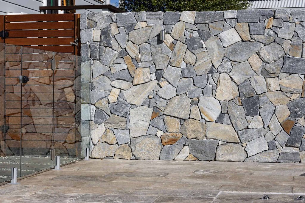 Dry stack stone feature wall from this pool landscaping Pokolbin project, with glass pool gate alongside