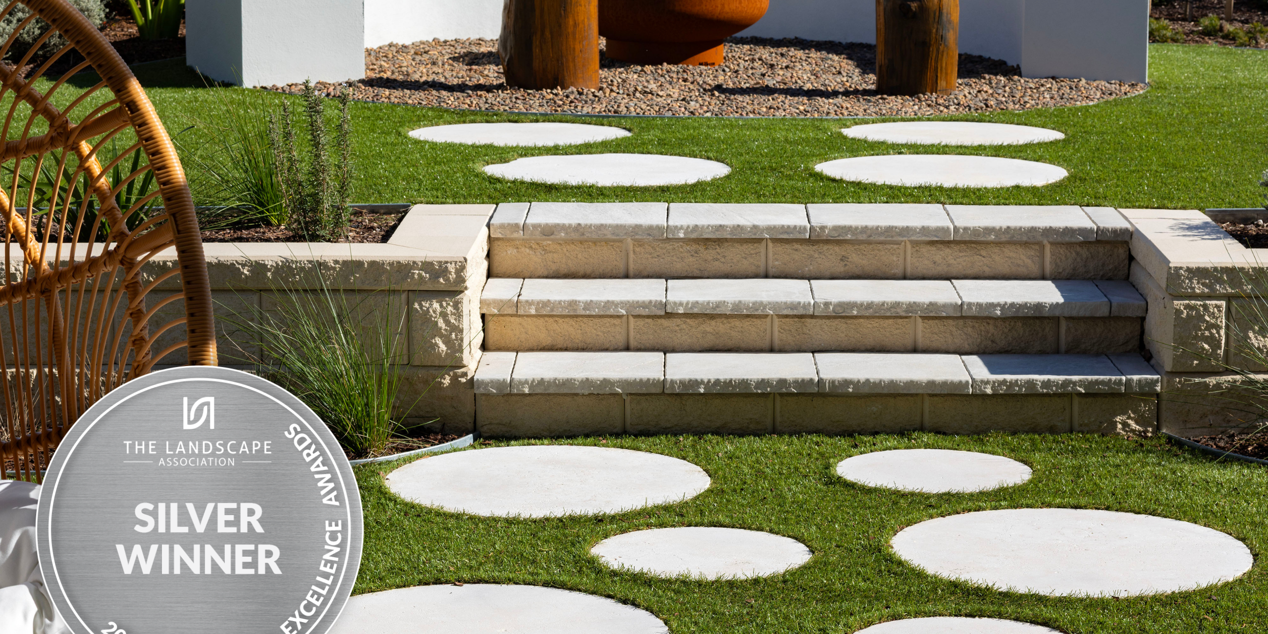 Domaine Display Home landscaping project in Cooranbong NSW, design and construct of an outdoor entertainment area, including a firepit, sandstone retaining wall with steps, steppers, concrete seating, and turfing.